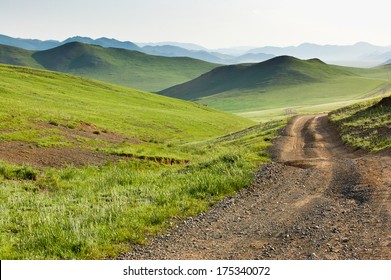 Winding Dirt Road Through Lush Rolling Hills Of Central Mongolian Steppe