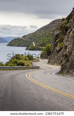 A winding mountain road lies in the foreground of a breathtaking landscape in Queenstown, New Zealand