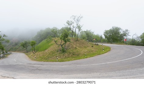 A winding mountain road with a sharp turn disappearing into thick morning fog