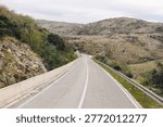 Winding mountain road under clouds. Empty asphalt route background. Rocky hills countryside scene. Scenic travel drive view. Remote landscape adventure. Guardrail curve detail.