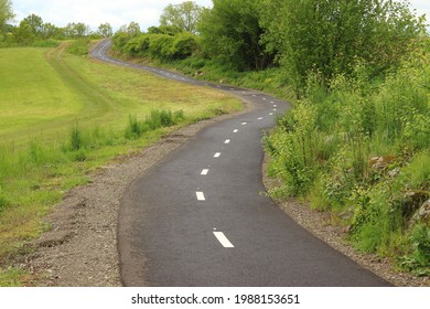 winding narrow asphalt road between fields and trees with a visible dashed line