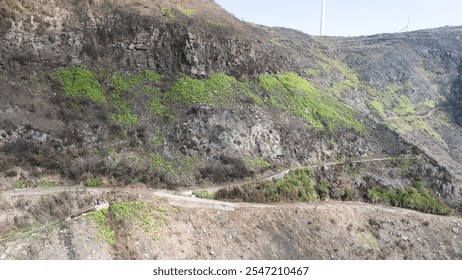 A winding path runs through a scenic mountain landscape, showcasing lush green vegetation and striking rock formations, under a clear sky. - Powered by Shutterstock