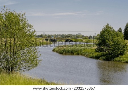 A winding river with a dam across its current.River, trees, green meadows in spring entourage under the blue sky. The city (Ostrowiec Swietokrzyski) can be seen in the background. 