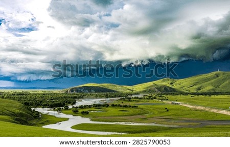 Winding river flows through green grassland, layered storm clouds fill sky, hills and woods stretch across vast wilderness.