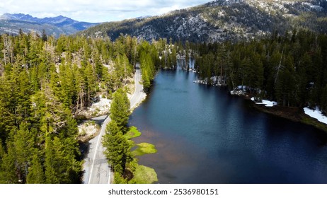 Winding Road Beside Serene Lake and Pine Forest in Mountains. A scenic winding road follows the edge of a serene lake surrounded by dense pine forests, nestled among mountainous terrain. - Powered by Shutterstock