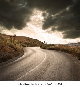 A Winding Road In Countryside With Gloomy Cloudscape At The Sunset