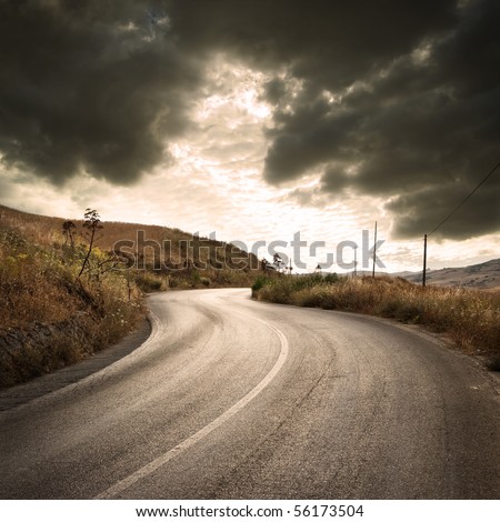 a winding road in countryside with gloomy cloudscape at the sunset