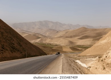 A winding road cuts through the barren terrain of Faryab Province, surrounded by rugged hills and valleys under a clear sky. Afghanistan - Powered by Shutterstock