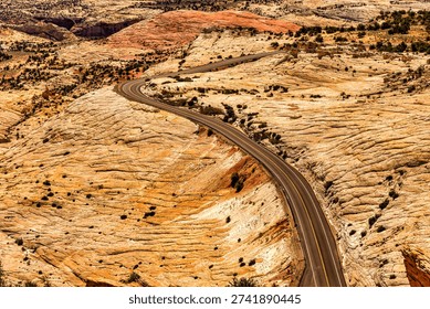 A winding road cuts through the dramatic, layered sandstone landscape of a desert canyon in Utah, showcasing the raw beauty of nature and the human endeavor to traverse it.
