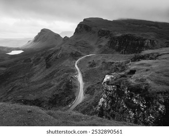 A winding road cuts through misty, rugged cliffs and hills under a cloudy sky, creating a dramatic, moody landscape. - Powered by Shutterstock