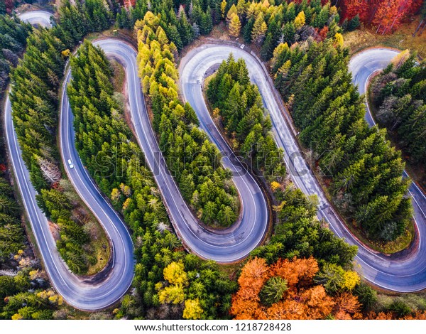 Winding road from high\
mountain pass, in autumn season, with orange forest. Aerial view by\
drone. Romania