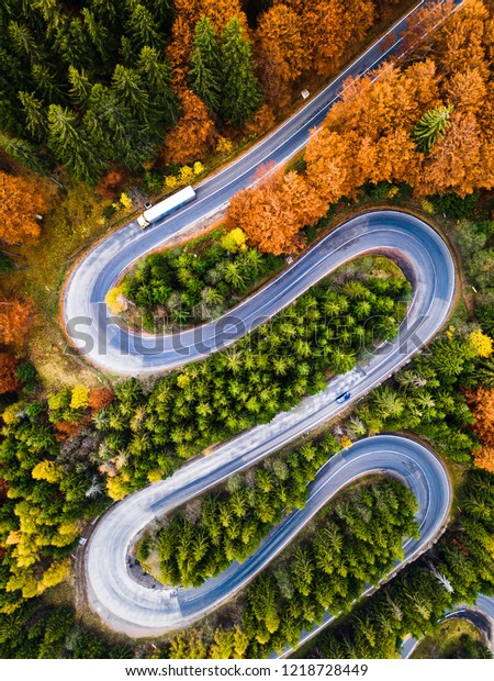 Winding road from high\
mountain pass, in autumn season, with orange forest. Aerial view by\
drone. Romania