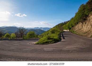 A winding road with a mountain in the background. The road is empty and the sky is clear