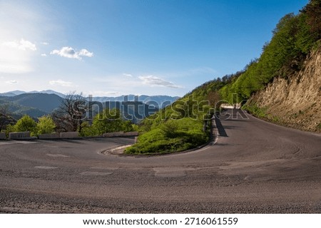A winding road with a mountain in the background. The road is empty and the sky is clear