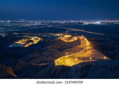 Winding Road In Mountains Against Illuminated City At Night. Al Ain In Abu Dhabi Emirate.
