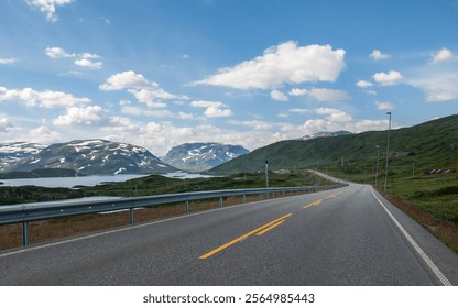 A winding road in Norway leads through a picturesque landscape of green hills and snow-capped mountains under a bright blue sky filled with fluffy clouds. This idyllic setting invites exploration. - Powered by Shutterstock