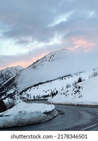 Winding Road On A Snowy Mountain Pass, Cloudy With Fog At Sunset.