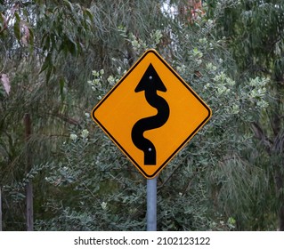 A Winding Road Sign To Warn Drivers To Slow Down In Preparation For Multiple Curves In The Road Ahead.