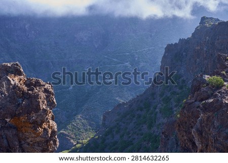 Winding road threading through the misty Masca gorge seen from a rocky ledge in the Teno massif