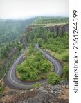 A Winding Road Through Forested Cliffs at Rowena Crest, Columbia river Gorge, Oregon curves through a lush green forested landscape with cliffs.