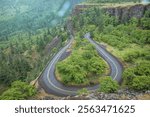 A Winding Road Through Forested Cliffs at Rowena Crest, Columbia river Gorge, Oregon curves through a lush green forested landscape with cliffs.