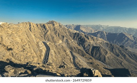 Winding road through rugged mountains, offering breathtaking scenic views, sharp turns, and stunning natural rock formations under clear skies.