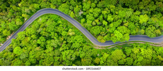 Winding road, top view of beautiful aerial view of asphalt road, highway through forest and fields in rainy season. For traveling and driving in nature. Banner panorama background
