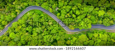 Winding road, top view of beautiful aerial view of asphalt road, highway through forest and fields in rainy season. For traveling and driving in nature. Banner panorama background
