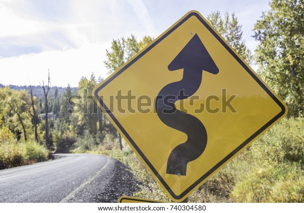 Winding road warning sign in front of a background\
including nature