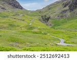 Winding steep road with some cars ascending to summit Hardknott Pass in Lake District National Park, Cumbria, UK