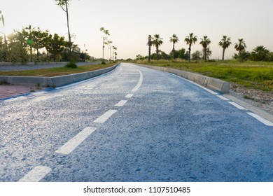 Winding Tarred Road With Middle Markings At Sunset In A Low Angle View With Palm Trees On The Skyline And A Glow In The Sky