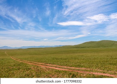 A Winding Track Across A Mongolian Grassland With Mountains And A Lake In The Background