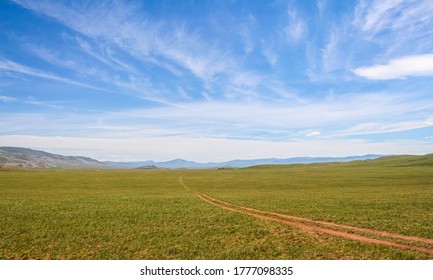 A Winding Track Across A Mongolian Grassland With Mountains And A Lake In The Background