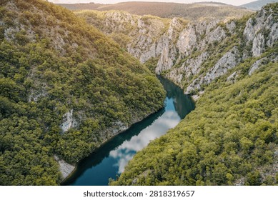 A winding turquoise river flows through a dramatic limestone canyon flanked by dense green forest, captured from above at golden hour.