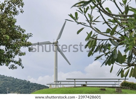 Windmill and blue sky, green grass hill background. Famous windmill installed on a small hill near solar panels insideWindmill Viewpoint at Nai Harn beach, Phuket, Thailand. 
