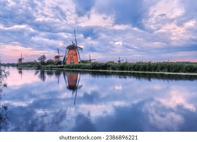 Windmill reflected in the water under a cloudy sky. Kinderdijk National Park in the Netherlands. Dutch canals.