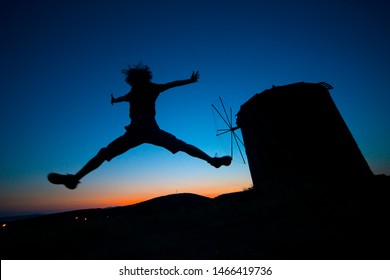 Windmill silhouette and jumping people in Sunsets./Cunda island,Ayvalik,Turkey