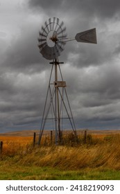 A windmill spins in the wind with angry clouds behind it.