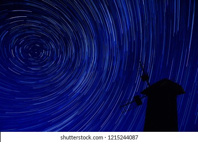 A windmill standing against the sky with a star trail