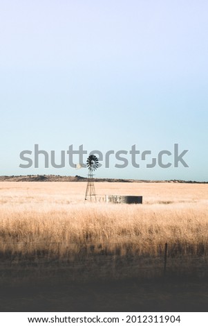 A windmill standing alone in the long grass of a dry and barren landscape 