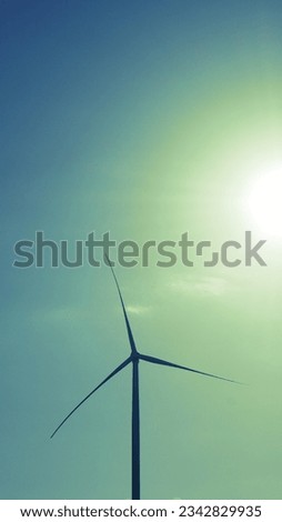 a windmill with three propellers generating dark wind power and a green sky and the sun during the day