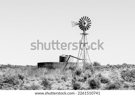 A windmill with a watertank inside an old corrugated iron dam on the road between Loxton and Fraserburg in the Northern Cape Karoo. Monochrome