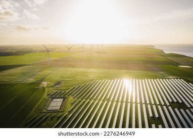 Windmills and solar panels farm in green fields close to the ocean. Renewable energies concept. Green energy for carbon dioxide emission reduction. 