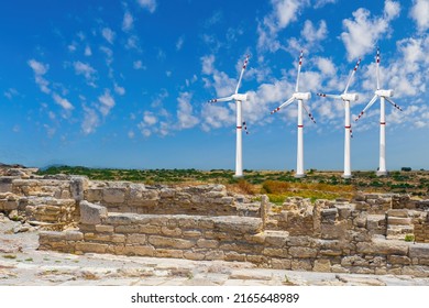Windmills in summer. Environmentally friendly power plant next to ruins. Walls of ancient building are electronic generators. Windmills are spinning on horizon. Generation of green electricity