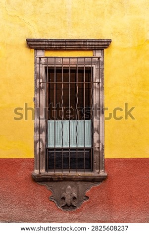 A window with bars and curtains is set in a yellow and red wall, showcasing architectural details and security measures.