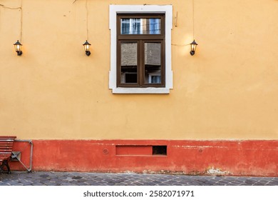A window with a bench in front of it. The bench is empty. The wall is yellow and the window is brown