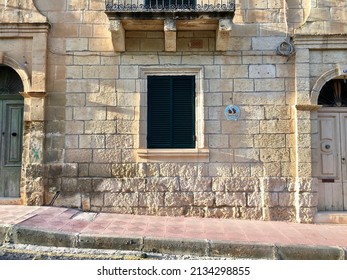 A Window With Black Shutters In A Sandstone House. Malta