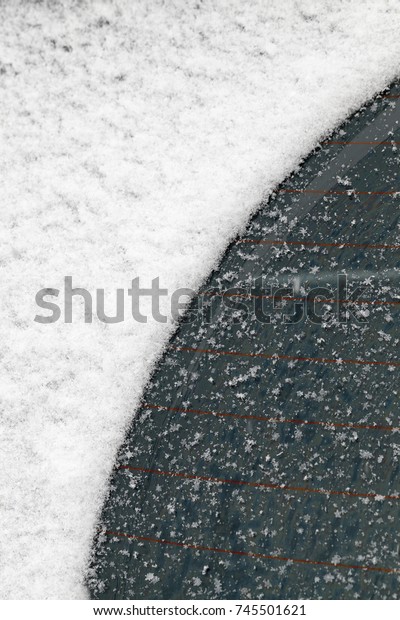 window of the car with heating threads. on the\
surface of the glass there are white snowflakes and a part of the\
snow has already melted and is cleaned by car wipers, the photo is\
close-up in winter