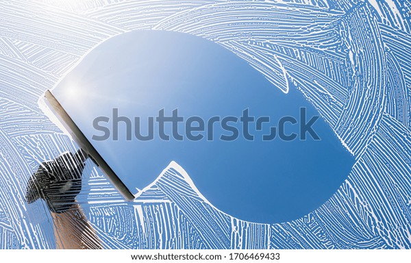 window cleaner cleaning window with squeegee and\
wiper on a sunny day