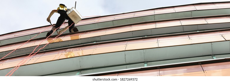 Window Cleaner Hangs On Rope And Washes Windows. Industrial Mountaineer Services Concept